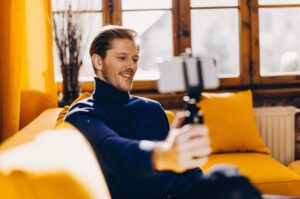 A young entrepreneur shoots video with his mobile phone in a warm home space