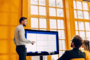 Νέος επιχειρηματίας της TWO DOTS παρουσιάζει την ιστοσελίδα σε συναδέλφους σε μοντέρνο γραφείο, δείχνοντας αξιοπιστία.