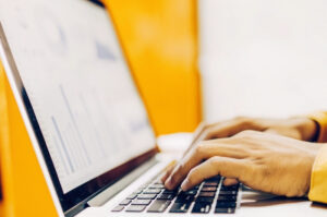 Close-up of hands typing on a laptop keyboard with charts and graphs for the campaign's performance
