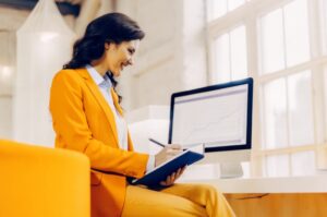 Γυναίκα επαγγελματίας σημειώνει οδηγίες SEO, έχοντας ανοιχτά αναλυτικά στοιχεία στη οθόνη της για καλύτερη κατάταξη στη Google