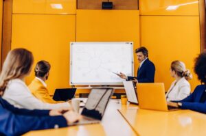 Επαγγελματίες και επιχειρηματίες συγκεντρωμένοι γύρω από ένα τραπέζι γραφείου, με φορητούς υπολογιστές και ψηφιακά tablets, συζητούν στρατηγικές μάρκετινγκ και σχεδιάζουν ένα μεγάλο διάγραμμα SEO σε έναν πίνακα