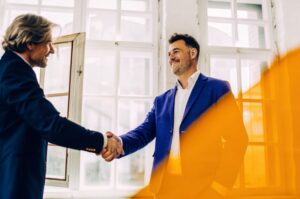 Δύο επιχειρηματίες ανταλλάσσουν χειραψία ως ένδειξη εμπιστοσύνης, αναδεικνύοντας τη σημασία της Gentlemen’s Agreement στις επιχειρηματικές συμφωνίες με το brand TWO DOTS